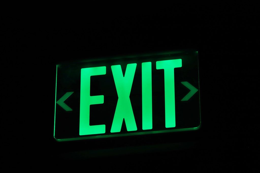 Illuminated green EXIT sign with directional arrows in a dark corridor