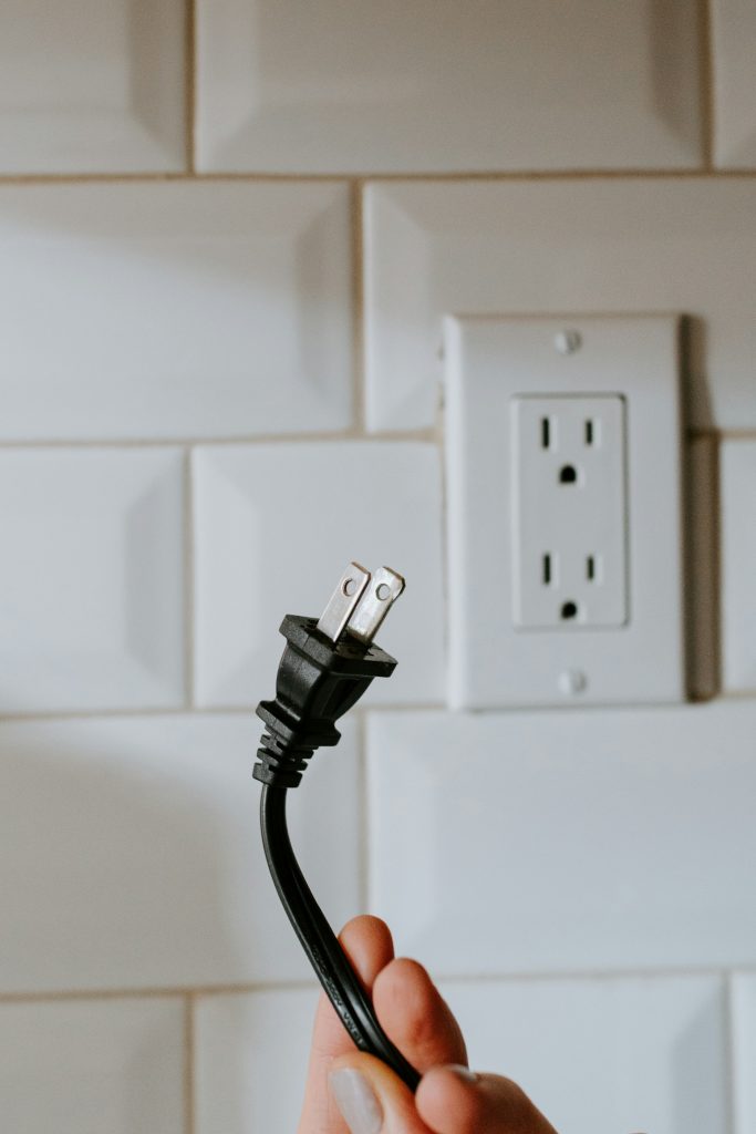 Standard duplex wall receptacle above a kitchen counter with a plug in hand
