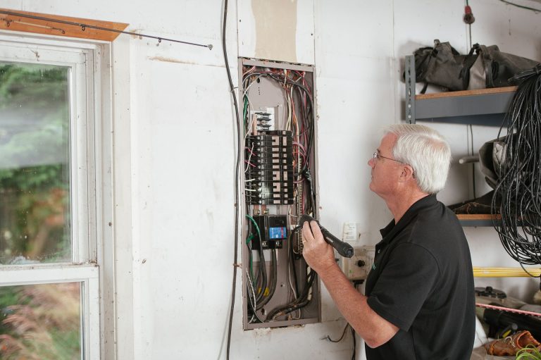 Electrician checking an open residential breaker panel with a flashlight