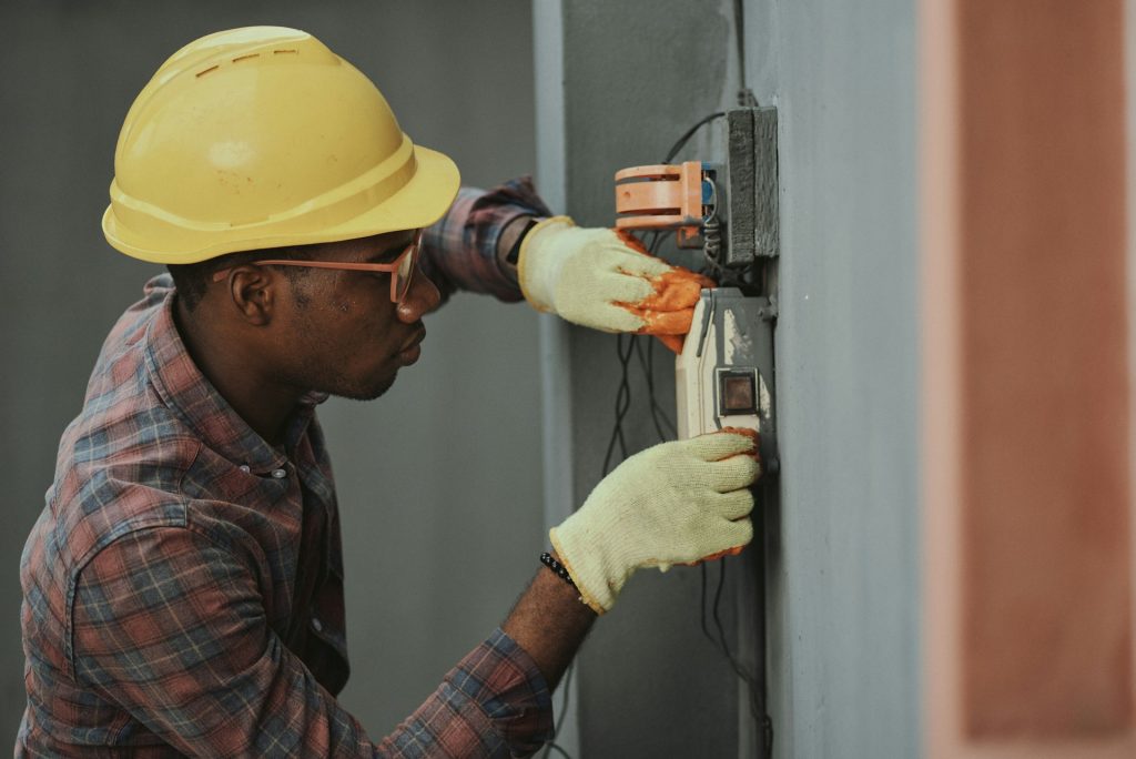 Electrician in a hard hat working on a wall-mounted electrical fitting